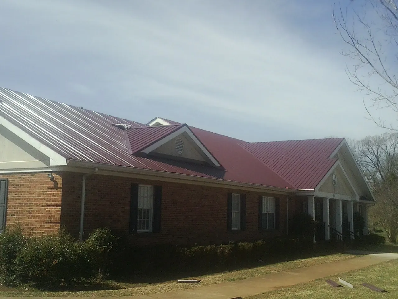 Red metal roof with gabled entries on a long brick building, from a Hail Damage Roof Repair job in Playa Vista