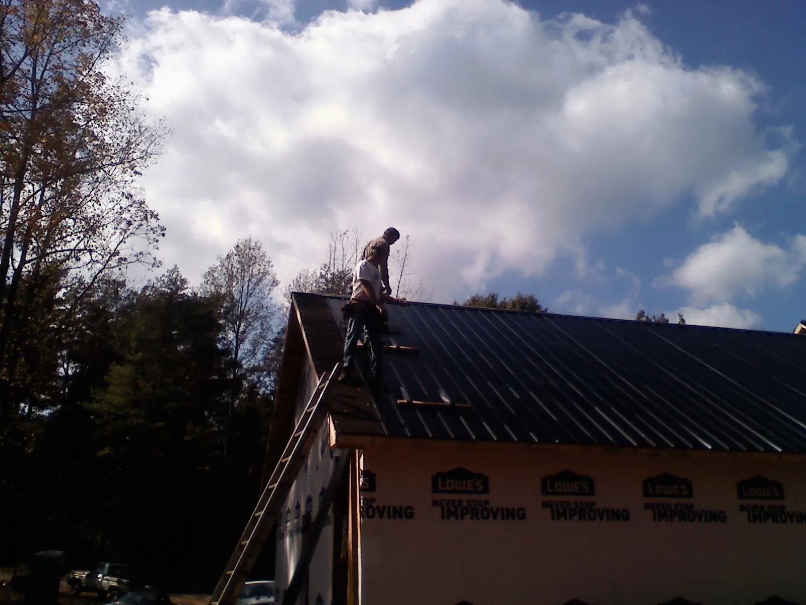 Roofer fastening dark metal panels high against a cloudy sky, from a Roof Inspection job in Playa Vista