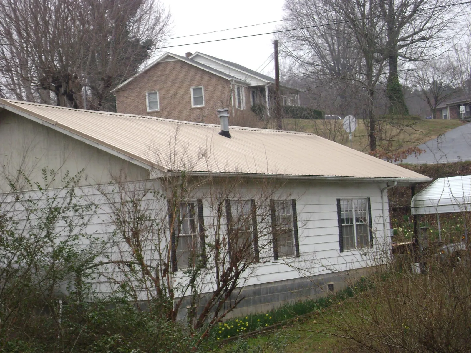 Tan metal roof on a white sided house set into a hillside — Commercial Roofing by Roofing Brothers in Playa Vista
